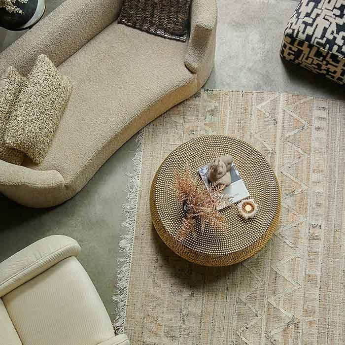 Dewitt Brass Stud Coffee Table, a large round coffee table covered entirely in small brass studs, in a natural-hued lounge.