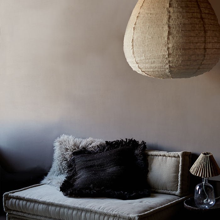 Relaxed look sofa with black and grey cushions in front of a mid tone chocolate painted wall
