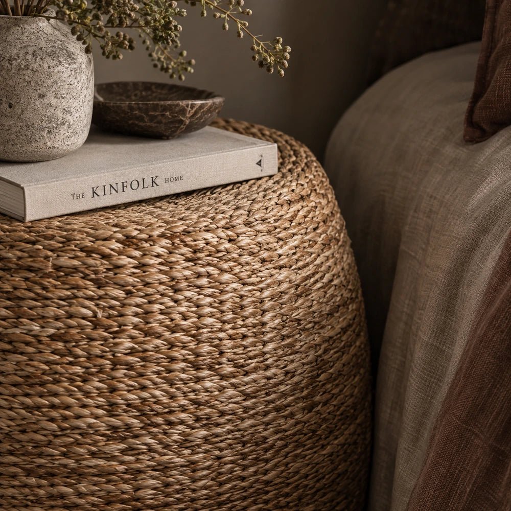 Elias Seagrass Stool shown close up beside a bed, highlighting its rounded woven texture, natural fibres and basket-like form within a softly styled bedroom.