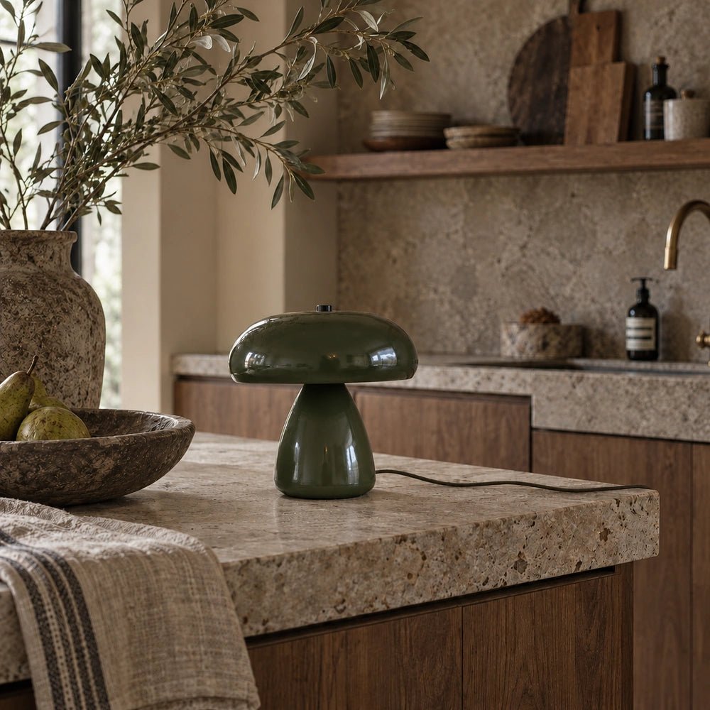 Elmore Metal Table Lamp viewed from the front with rounded olive shade and glowing bulb, styled on a stone island in a warm contemporary kitchen.