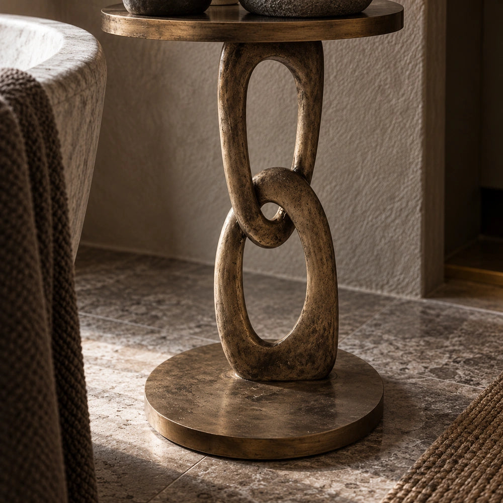 Emilio Side Table shown close up with its sculptural linked pedestal, rounded tabletop, textured vase and decorative objects beside softly layered neutral bedding.