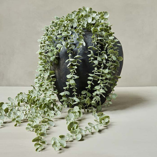 Fake eucalyptus foliage trailing out of a black stoneware vase.