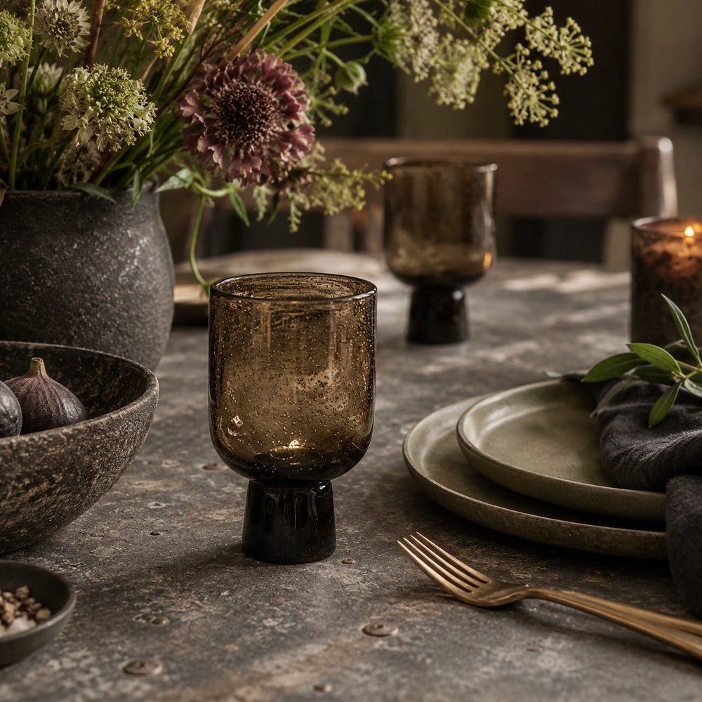 Evie Glass, Burnt Umber shown close up in a dining table setting, with its warm textured bowl and dark pedestal surrounded by layered tableware.