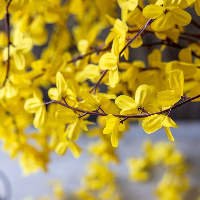 Detail of the yellow fabric petals on a stem of artificial forsythia.