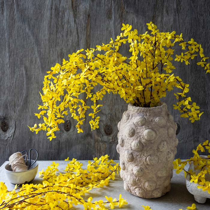 A bouquet of vibrant yellow artificial forsythia arranged in a bobble textured vase.