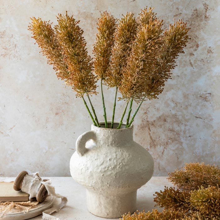 An artisan style vase with a cream ceramic textured glaze, styled with a bunch of textural faux foliage.
