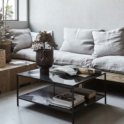 A square coffee table in black metal finish, with a low storage shelf beneath the table top.