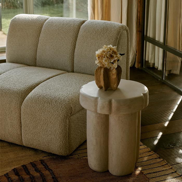 Styled image of a curved, organically shaped cream side table with a small vase of artificial flowers and a large cream occasional chair.