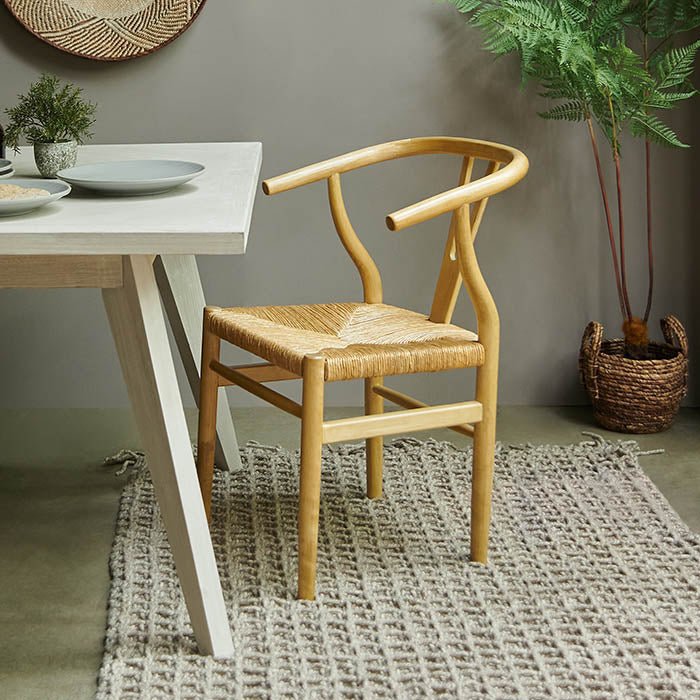 Wooden dining chair with straw seat, in natural light brown colour, next to white-wash dining table.