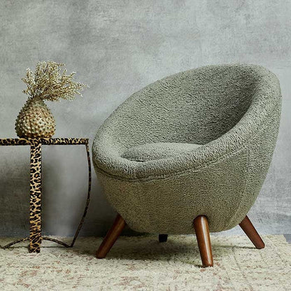 Round armchair with four wooden legs in a grey boucle fabric next to a leopard print table
