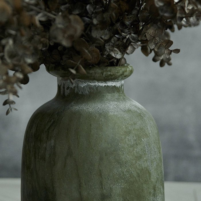 Frosted green glass bottle vase filled with brown eucalyptus