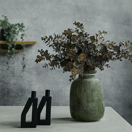 Frosted green glass vase filled with a large bunch of eucalyptus sat next to two black candlholders