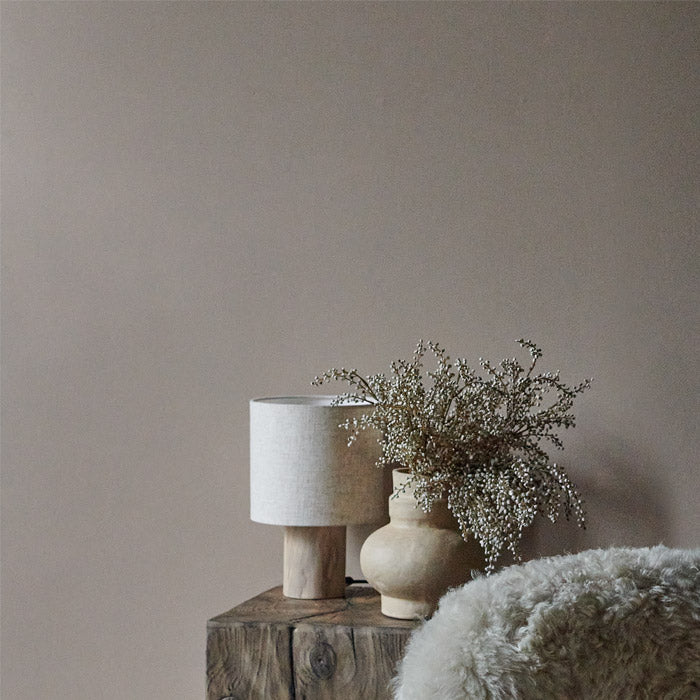 A close up of a Haze painted wall styled with a faux fur accent chair, a wooden side table and a vase with some faux botanicals.