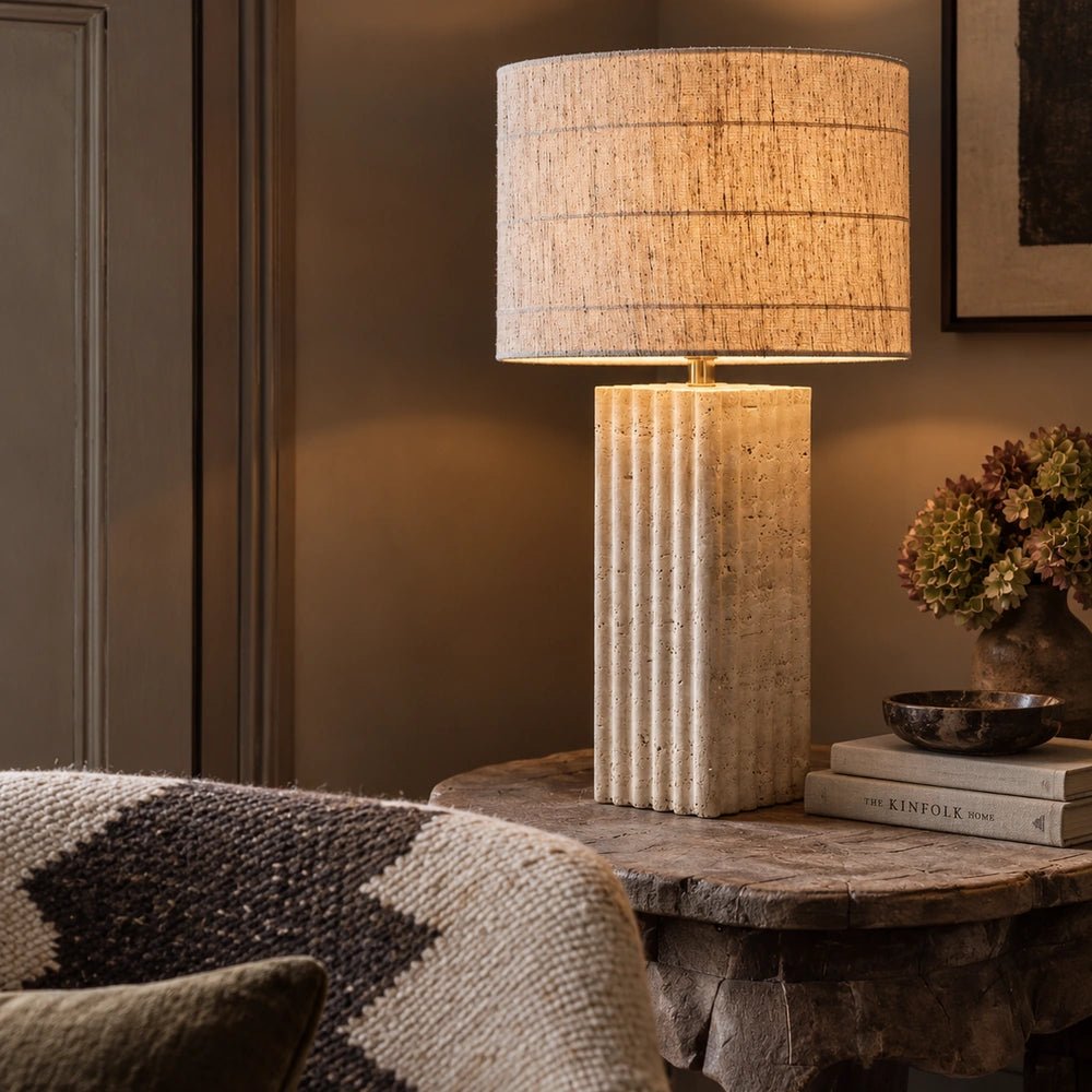 Hurdcott Travertine Table Lamp with pale stone base and rounded shade, styled on a console beside artwork and decorative objects in a neutral interior.