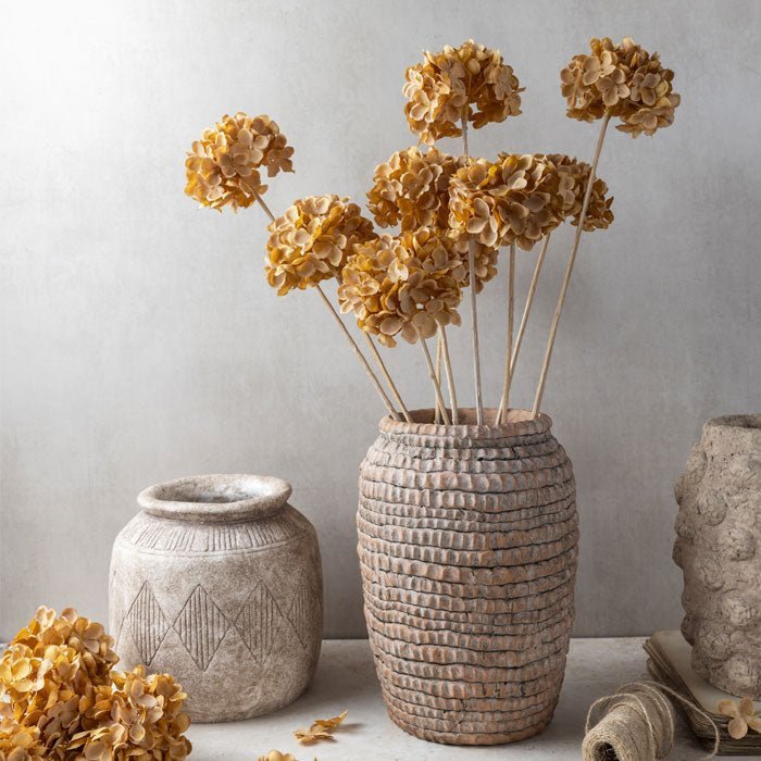 A rustic bobble textured ceramic vase with some fake flowers in it next to a smaller ceramic vase.