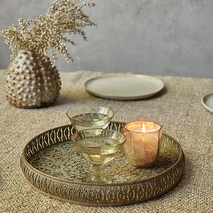 Gold patterned metal tray with two champagne glasses and a lit candle on top