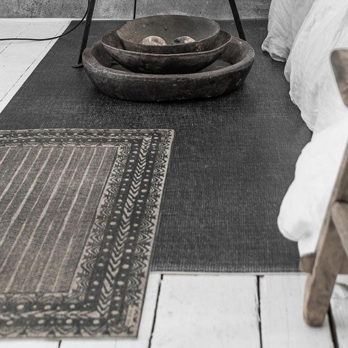 Two different patterned grey vinyl rugs placed on top of eachother on white wooden floorboards