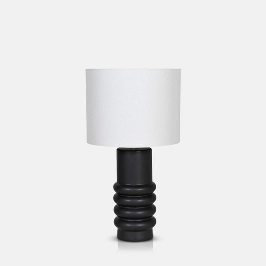 Table lamp with black ceramic base, with sculptural ribbed detail, and white drum shade.