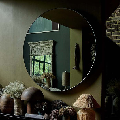 A large round mirror with a thin black frame hung on a wall