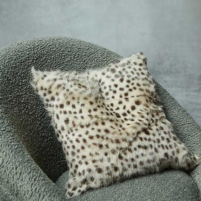 The Kampala Leopard Print Cushion, a small square cushion with a leopard print design on a goat fur front, on a grey-green chair.
