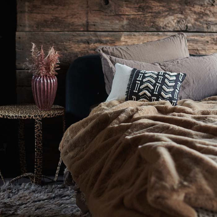 The Kanan Throw, a super soft faux fur caramel brown throw spread across a bed with cushions.