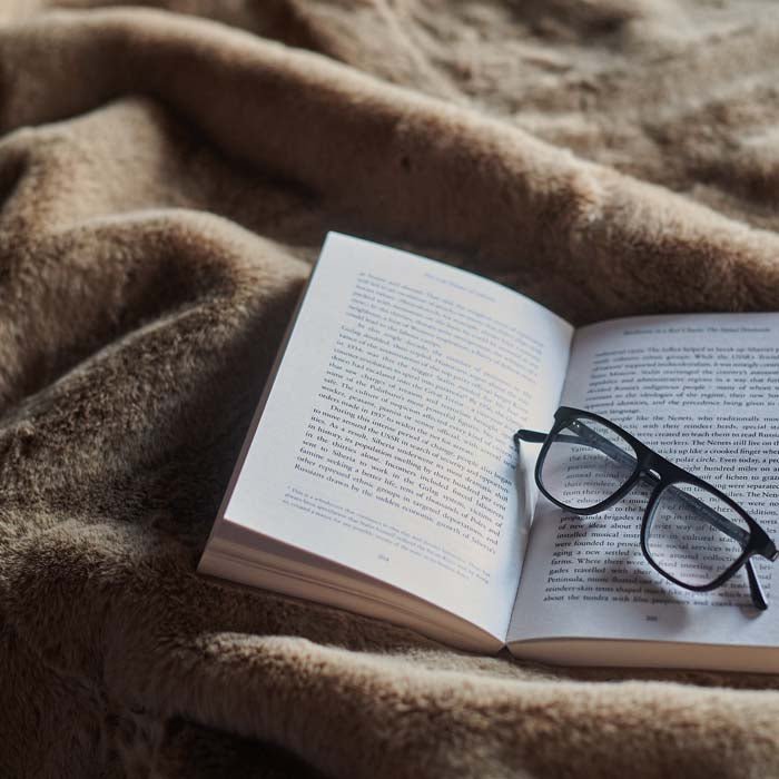 The Kanan Throw, a soft brown faux fur throw displayed with a book and reading glasses.