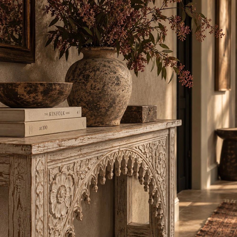 Karnata Carved Console with ornate carved front and dark finish, styled beneath artwork with lamps and decorative objects in a warm neutral hallway.
