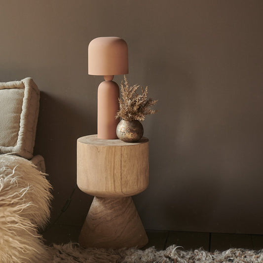 Pink table lamp sat on a wooden table in front of a warm brown painted wall