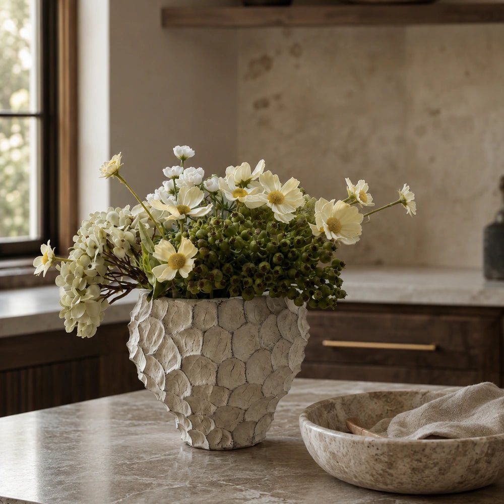 Ladris Cement Vase with textured sculptural surface, filled with cream flowers and green stems on a stone kitchen island in a warm neutral interior.