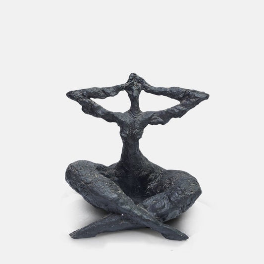 A cutout of a large resin sculpture, in matte black finish, depicting a cross-legged seated figure with its arms raised to touch its head.