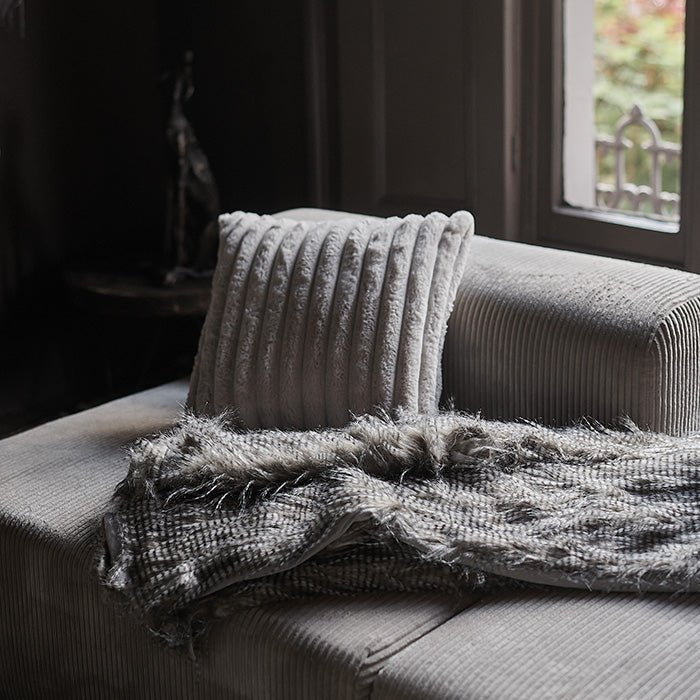 The Malton Throw draped across a sofa with a cream coloured cushion.