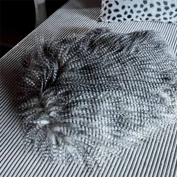 The Malton Throw, a faux fur throw with a thin black strip folded on a chair.