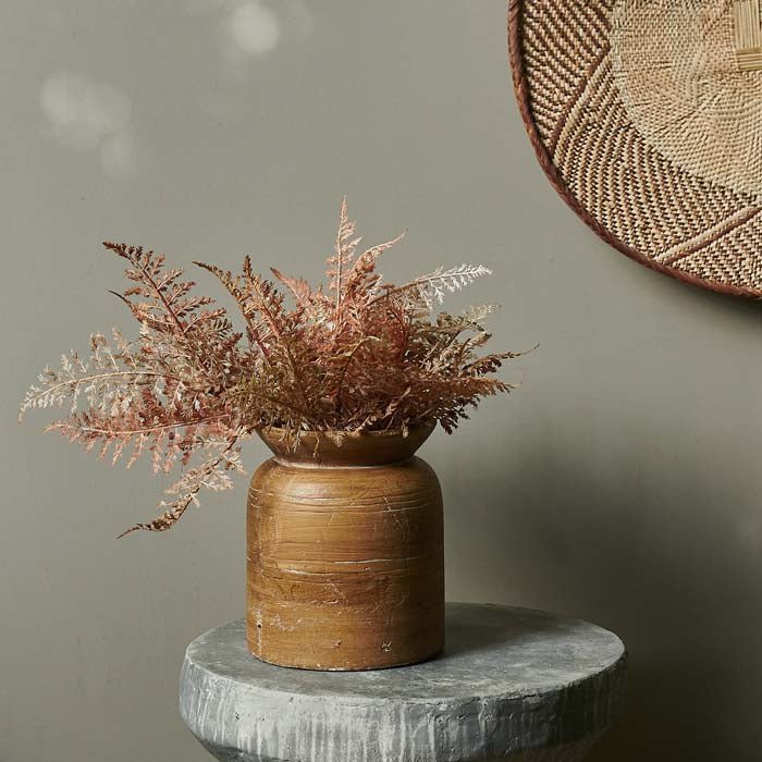 Textured round brown vase filled with a large bunch of orange fern stems in a faux bouquet