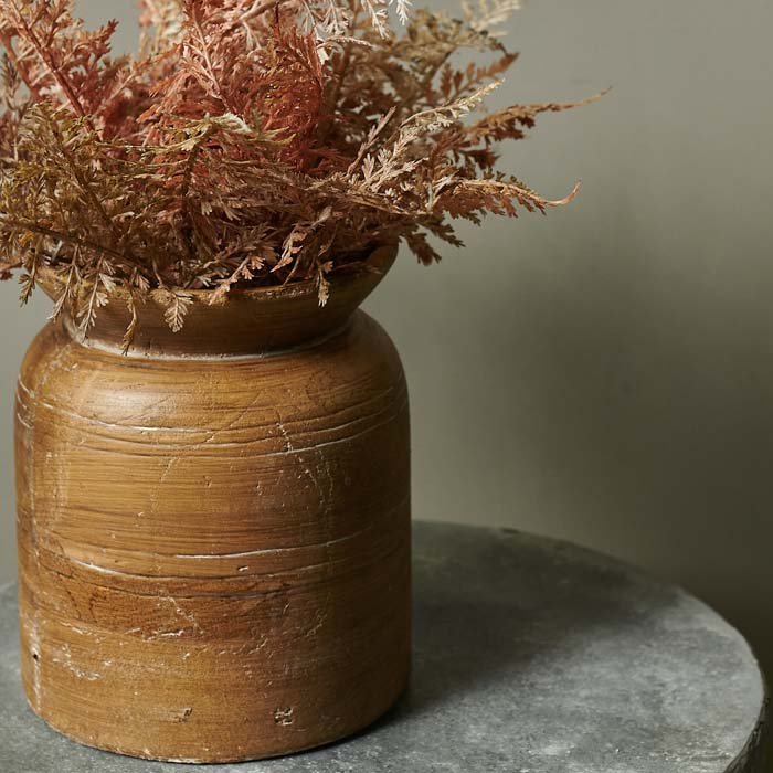 Round brown ceramic vase with rustic texture sat on a round grey table, a good example of how to arrange artificial flowers