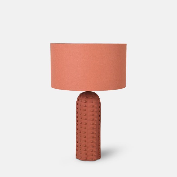 A cutout of the Maynard Table. A coral hued linen shade and a bubble textural ceramic matte base table lamp.