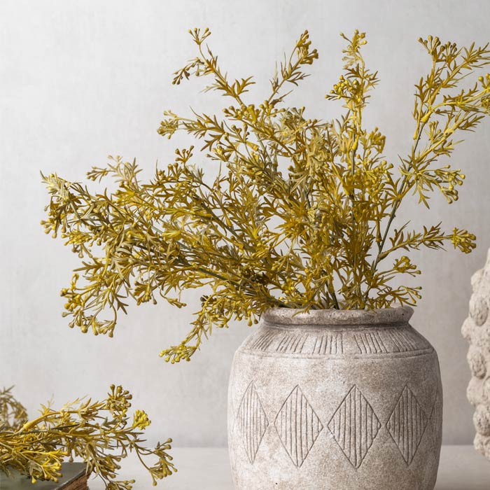 A bouquet of artificial meadow grass flaxen in a warm yellow colour, arranged in an engraved ceramic vase.