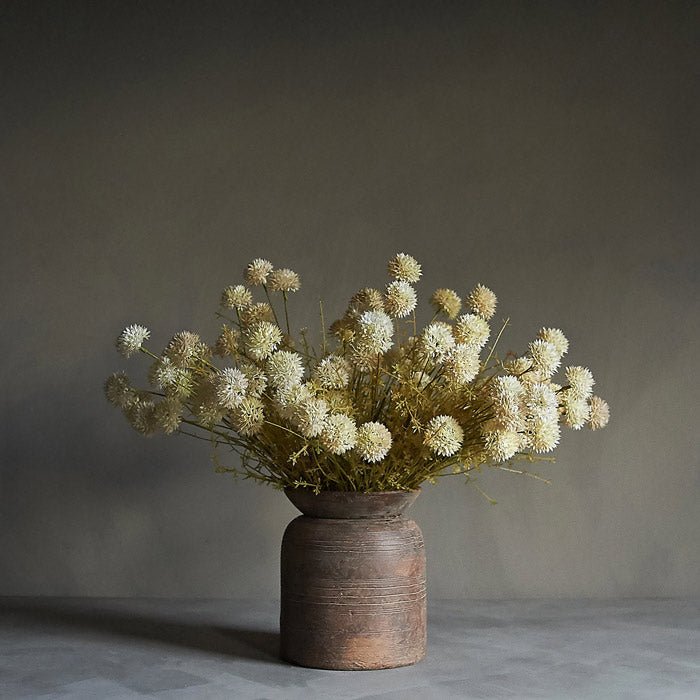 A ceramic vase full of artificial melaleuca cream flower stems arranged in a floral bouquet.