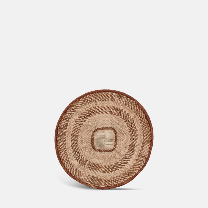 A cutout of the Melina Basket, a circular shallow woven basket with a geometric tribal pattern.