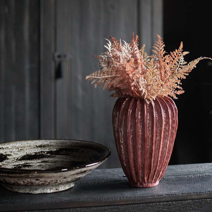 Mollie Ceramic Vase, a rective glazed ceramic vase with a ribbed texture in a dark pink hue styled with some rusty ferns.