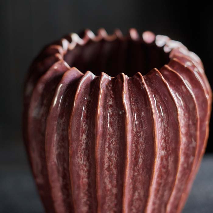 A close up of the Mollie Ceramic Vase. A rective glazed ceramic vase with a ribbed texture in a dark pink hue.