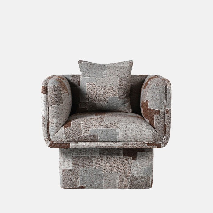 A cutout of the Monmouth Arnchair, a large boxy armchair on a pedestal with a patchwork pattern in grey-brown tones.