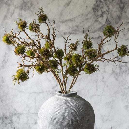Tall artificial mossy branches in a large stoneware vase.