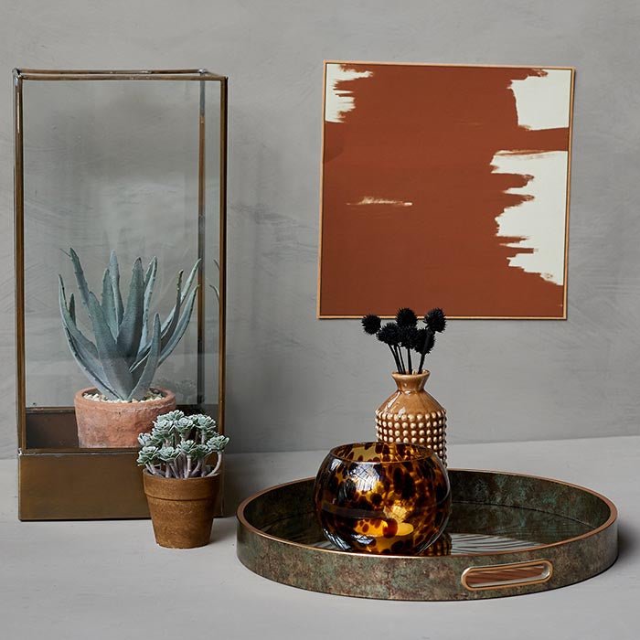 Abstract orange paint print in square frame hung above a gold tray