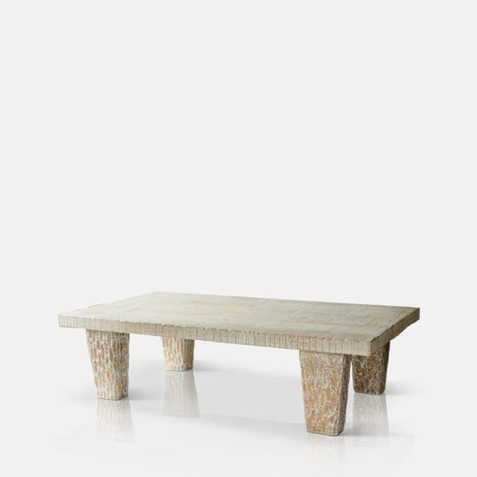 Cutout image on a white background of a pale coffee table. This wooden coffee table has four legs with a carved design.