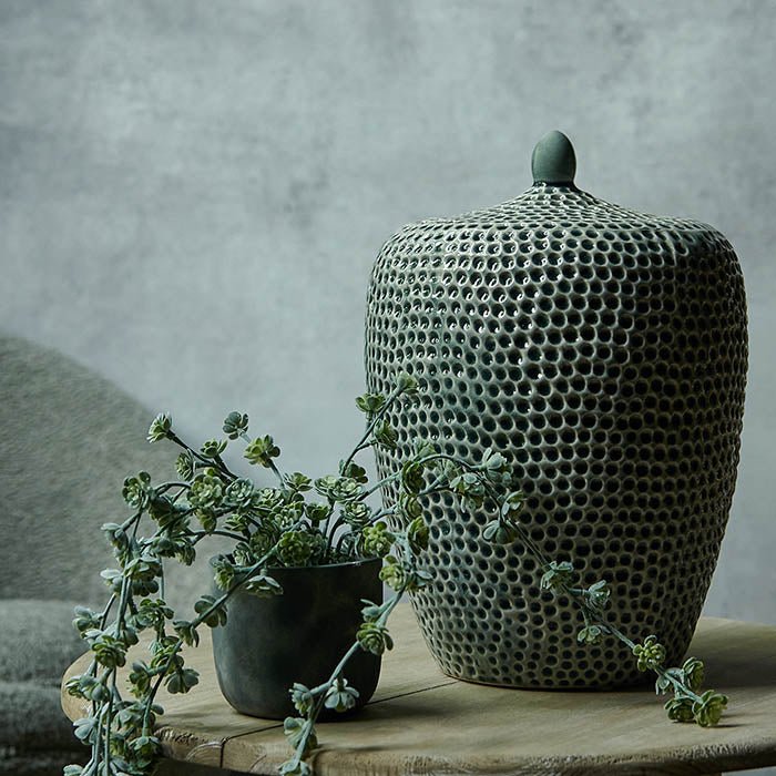 Honeycomb textured large green storage jar sat on a wooden table next to a potted plant