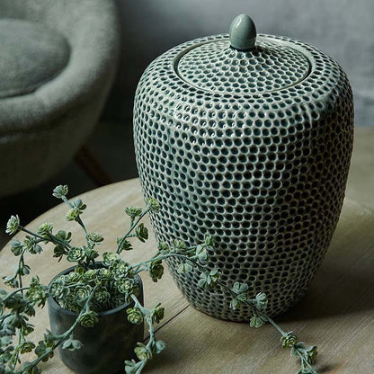 Large green storage jar covered in a honeycomb texture sat on a wooden table