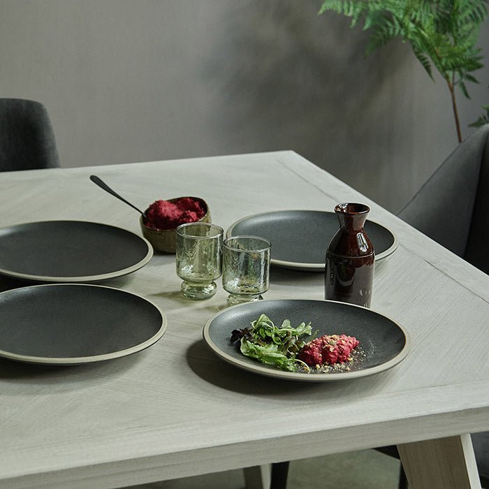 Bronson Parquet Dining Table, a rectangular herringbone wooden dining table styled with a set of black plates.