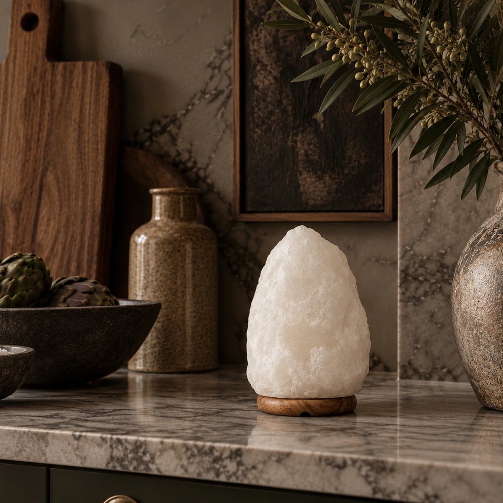 Nepal Natural Salt Lamp in white with a softly glowing sculptural stone form, displayed on a dark side table beside a neutral sofa and textured cushions.