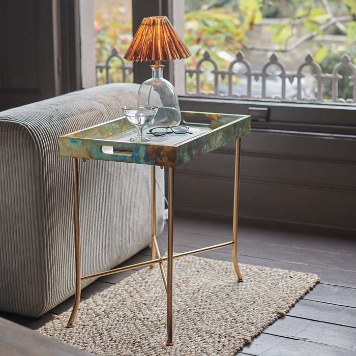 Rectangular metallic side table with aged patina, next to corduroy sofa.