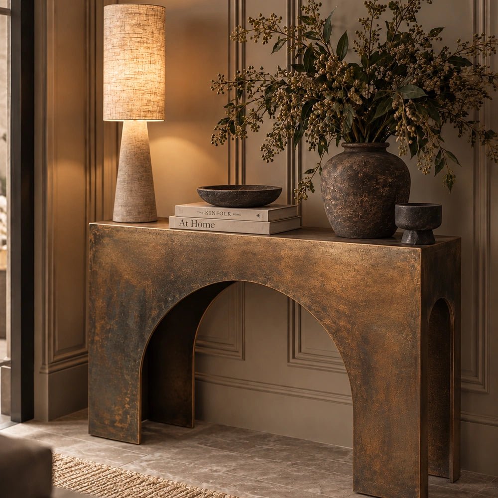 Orcheston Metal Console Table with a slim dark frame and textured surface, styled with decorative vessels and branches in a warm neutral hallway interior.